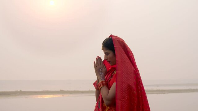 Woman joining hands and praying to Lord Sun on the festival of Chhath Pooja - Chhath Mahaparv  Chath Puja rituals. Shot of a woman in a traditional Chhath Pooja attire standing in the river - worsh...