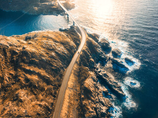 Aerial view of bridge, car, sea with waves and mountains at sunset in Lofoten Islands, Norway....