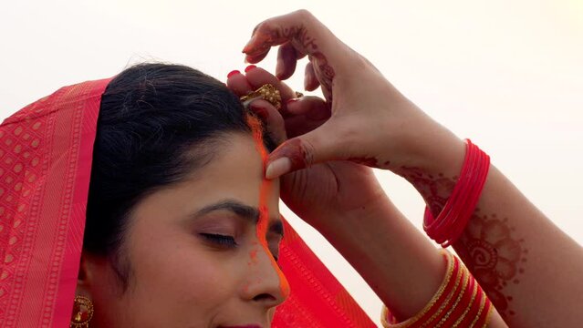 Closeup shot of a woman applying sindoor in a ritual for Chhath Pooja - religious festival  offering prayer to Lord sun. Beautiful young woman celebrating the festival of Chhath Pooja in the mornin...