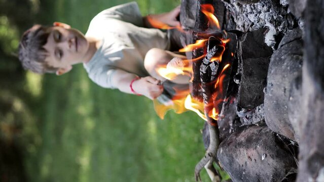 Little boy sitting near bonfire grilling marshmallow on stick dropping.
