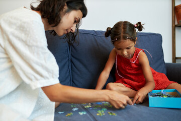 Side view portrait of baby sitter playing puzzle game with little lovely girl in red dress and...