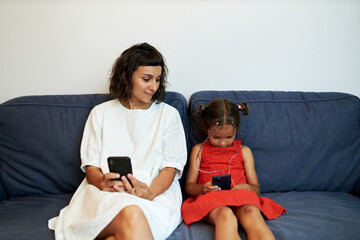 Mom and daughter using smartphones sitting on couch, pretty woman browsing social media, funny...