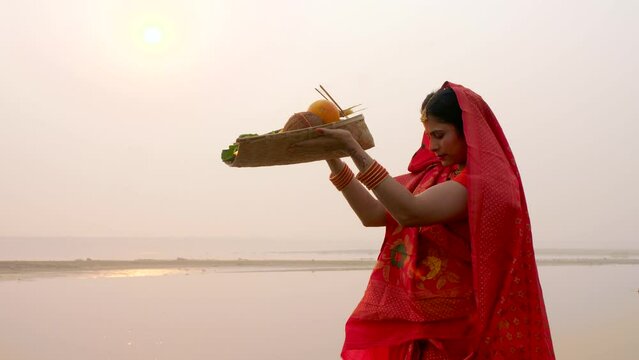 A woman offering prasad  fruits  vegetables  and other items and a Diya to pray sun God at a lake during Chhath Puja. Hindu devotees worship God sun with a ritual while standing in a river - Hindu ...