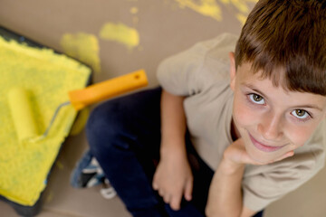 A boy in a construction uniform sits near paint paints. Repairs. Painting the walls