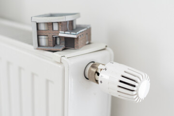 House model wrapped in scarf on radiator indoors, space for text. Winter heating efficiency