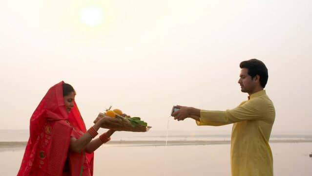Traditionally dressed man and a woman - Chhath pooja  worshipping Lord Sun  offering Prasad  offering water  Indian rituals. A couple offering prasad in a bamboo soop on an auspicious day of Chath ...