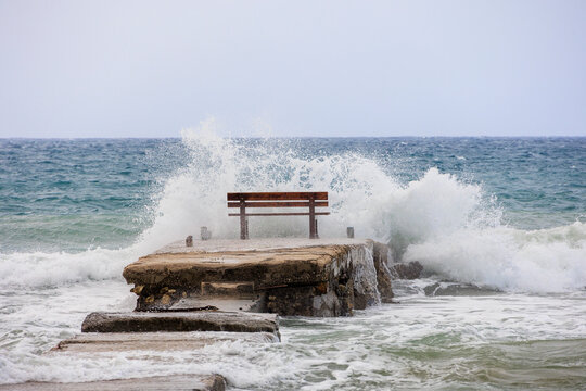 A resting bench in the middle of the waves on the island of Corfu near the town of Arillas under blue skies and heavy seas