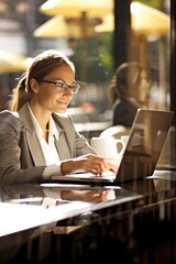 Young Caucasian businesswoman in eyeglasses works diligently seating at table with laptop in bustling cafe. Beautiful woman work online with laptop in lively cafe.