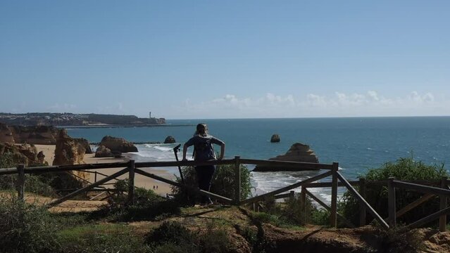 Mulher nova parada encostada a uma veda&ccedil;&atilde;o olhando o mar azul.