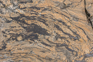 Background pattern from a brown granite stone. Unstructured lines of the surface. Dark color breaks with slight structural breaks. some gray color elements in the natural stone