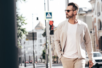 Fototapeta na wymiar Portrait of handsome confident stylish hipster lambersexual model. Sexy modern man dressed in elegant suit. Fashion male posing in the street background in Europe city at sunset. In sunglasses. Walks