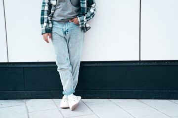 Man in casual street style clothes posing in the street. Model in blue jeans, shirt and sneakers stands near wall. Unrecognised, no face - Powered by Adobe