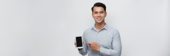 Smiling young man holds a modern smartphone in his hand and shows his finger on a blank screen - 672161510