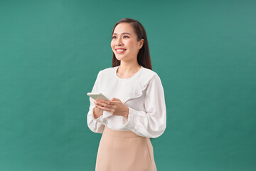 Portrait of a smiling casual woman holding smartphone over green background