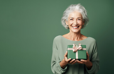 Beautiful mature woman 50, 60, 70 years old on a green background holding a large gift box, holiday surprise, compliment bonus for birthday anniversary