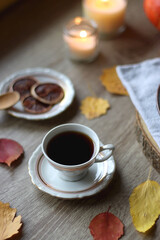 Cup of tea or coffee, plate with desserts, dried oranges, bowl of grapes, scented candles, vintage books, pumpkins and autumn leaves on the table. Autumnal hygge. Selective focus.