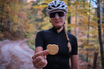 Female cyclist wearing cycling kit holding cookie snack for endurance during bicycle training.Sport...
