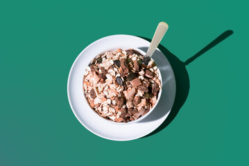 Cereal de granola muesli en un tazón blanco con cuchara sobre fondo verde. Vista superior
