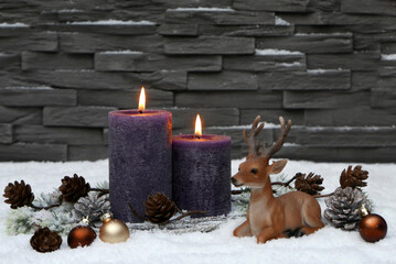 Zwei lila brennende Kerzen in einer Winterkulisse vor einer Steinmauer mit Platz für Text.