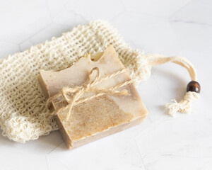 Beige handmade soap bar on soap saver bag on a marble table close up, mockup