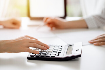 Fototapeta premium Two accountants using a calculator and laptop computer for counting taxes at white desk in office. Teamwork in business audit and finance