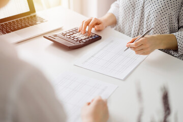 Accountant using a calculator and laptop computer for counting taxes with a client or a colleague at white desk in office. Teamwork in business audit and finance - obrazy, fototapety, plakaty