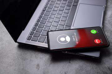 Smartphone laying on laptop while reciving unwanted call. Spam, scam, phishing and fraud concept. Security technology. - obrazy, fototapety, plakaty