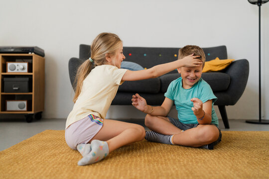 Cheerful girl in casual clothes practicing Lotus Pose with brother on carpet in living room at home