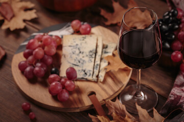 Glass of red wine served with blue cheese on dark wooden background. Autumn picnic with wine and cheese platter, fruits and dry leaves in rustic style