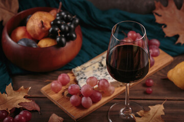 Glass of red wine served with blue cheese on dark wooden background. Autumn picnic with wine and cheese platter, fruits and dry leaves in rustic style