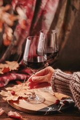 Autumn still life with two glasses of red wine and dry leaves in rustic style on dark wooden background. Womans hand holding glass. Romantic sweater weather, wine tasting concept