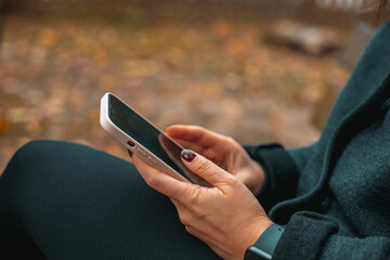 City lifestyle stylish  using a phone texting on smartphone app in a street. Young woman with smartphone in hand close-up.