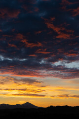 Stunning sunrise with beautiful shades of orange, pink, purple and blue colors with the silhouette of a mountain range. Wallpaper, natural background with copy space.