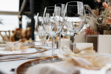 Transparent wine glasses on white tablecloth with plates and cutlery. Luxury restaurant close up view.