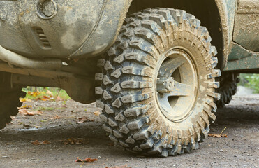 Wheel closeup in a countryside landscape with a mud road. Off-road 4x4 suv automobile with ditry body after drive in muddy road area