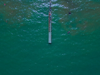 Aerial top down view of a wooden  pier in the sea. Wooden pier and people. Pier of Rimini, Italia, Emilia-Romania. Top aerial view from drone to seascape. Natural marine background with  waves. - obrazy, fototapety, plakaty