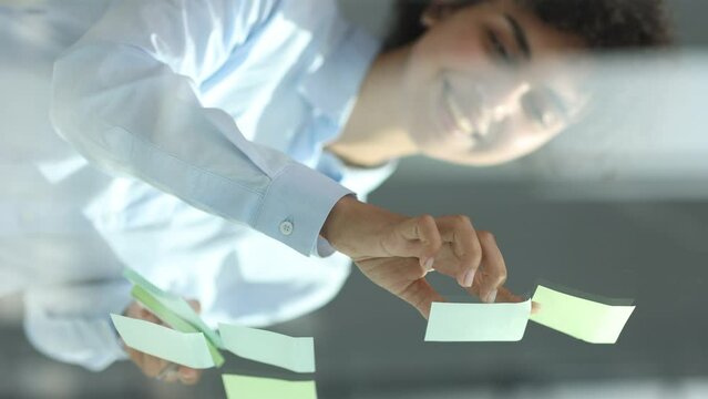 a girl in a modern office behind glass uses sticky notes and makes notes
