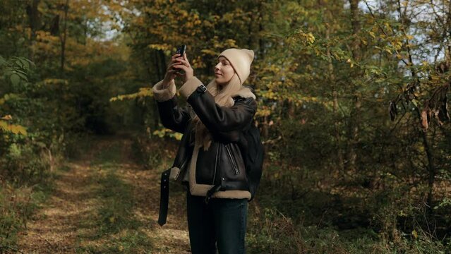 Young Woman Tourist in Autumn Forest Taking Pictures with Smartphone. Walking Women in the Autumn Forest, Enjoying the Nature