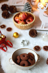 Cup of tea or coffee, glass of wine or juice, bowl of cookies, organic pomegranate, fluffy blanket, pine cones, various Christmas decorations and lit candles on the table. Christmas hygge concept.