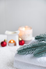 Fototapeta na wymiar Fresh white towels with fir branch, candles and Christmas decorations. Skin care and body care. SPA massage or beauty salon, relaxation and self care in Christmas or New Year variant. Copy space.
