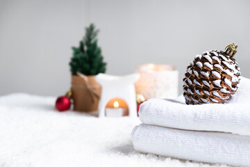 Fototapeta na wymiar Fresh white towels with candles and Christmas decorations. Wellness and wellbeing. SPA massage or beauty salon, relaxation and self care in Christmas or New Year variant. Copy space.