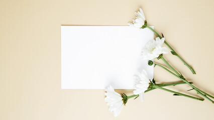 Empty white paper blank, flowers on beige background. Wedding branding mock up. Top view. Copy space
