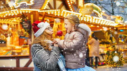 Obraz na płótnie Canvas Happy mother and daughter eat a red sugar apple at the traditional German Christmas market.