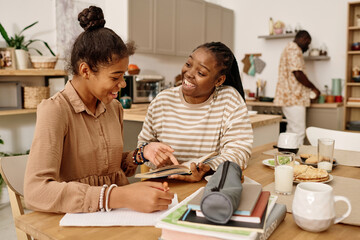 Cheerful mother helping teenage girl with doing homework