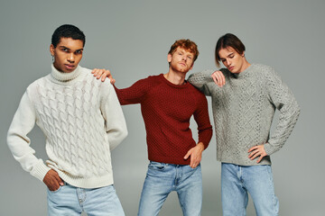 stylish interracial male models in vibrant casual sweaters posing on gray backdrop, men power