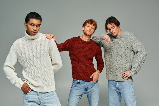 stylish interracial male models in vibrant casual sweaters posing on gray backdrop, men power