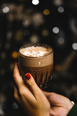 Beautiful young woman in a green knitted sweater with a mug of hot cocoa and marshmallows near the Christmas tree. New Year