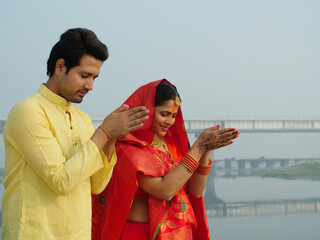 A couple worshipping Lord Sun at sunrise and celebrating the Chhath Pooja - auspicious day  Bihari...
