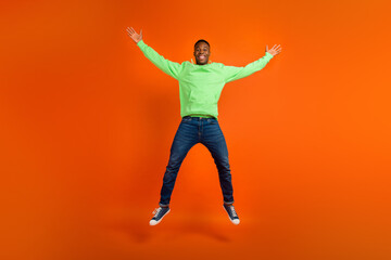 Fototapeta na wymiar Full body photo of satisfied funky guy dressed green hoodie denim pants jumping demonstrate big sale isolated on vivid orange background
