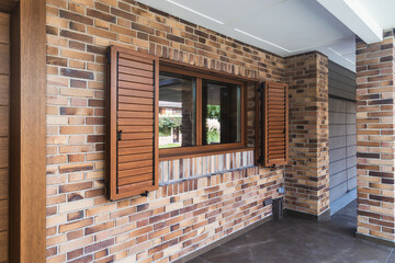 Brick facade of a house with window and wooden shutters. Side view. Design concept and quality materials.